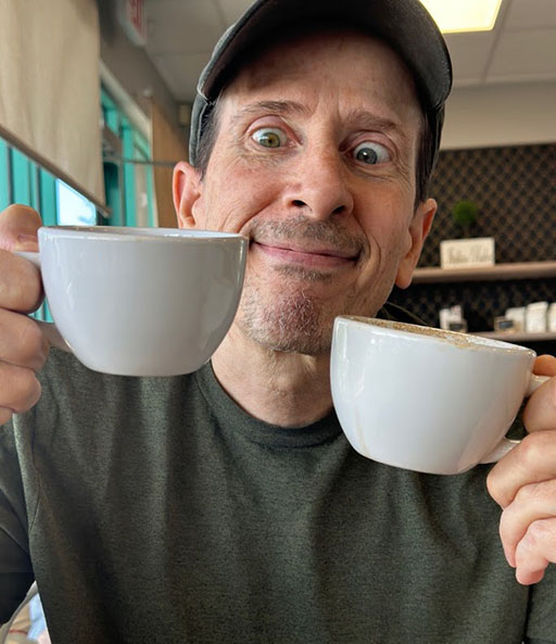 Image of a weird man excitedly holding two cups of coffee